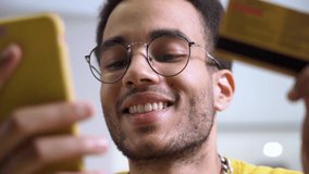 A smiling young African-American man with a credit card and a smartphone. A happy shopper making a purchase at an online store using instant and easy mobile payments. Electronic banking app service - Powered by Shutterstock - Get 15% off with code: PIKWIZARD15