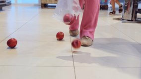 Video of apples spilled out of the bag on the floor in the store and woman hands picked up all the apples.