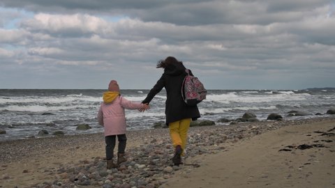Mother and daughter wearing warm outfit spending time together on a beach in winter.