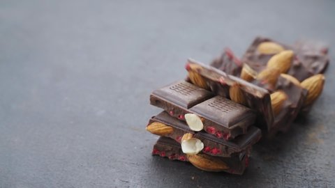 almond tower nuts falling on chocolate bar. Cooking chocolate bars with almonds, raspberries, handmade sweets. bars and pieces dark chocolate on black background. Confectionery craft on table