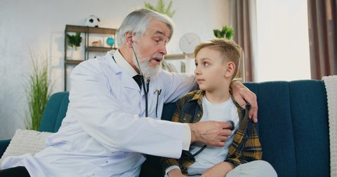 Doctor's home visit concept where likable confident friendly high-skilled respected doctor examining boy patient's breath using stethoscope,front view,slow motion