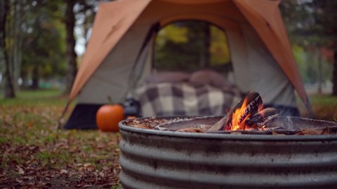 closeup of campfire with tent in background on fall camping trip