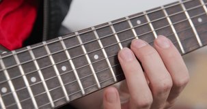 Person fingers the frets along the neck and presses strings, playing chords on an electric guitar, close up. Rehearsal before concert or learning to play musical instruments.