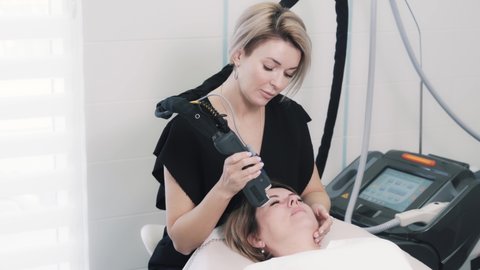 Front view of cosmetologist making anti-aging procedure for Caucasian woman. Hardware laser treatment makes skin smooth and shiny. Concept of modern technologies and beauty. High quality 4k footage