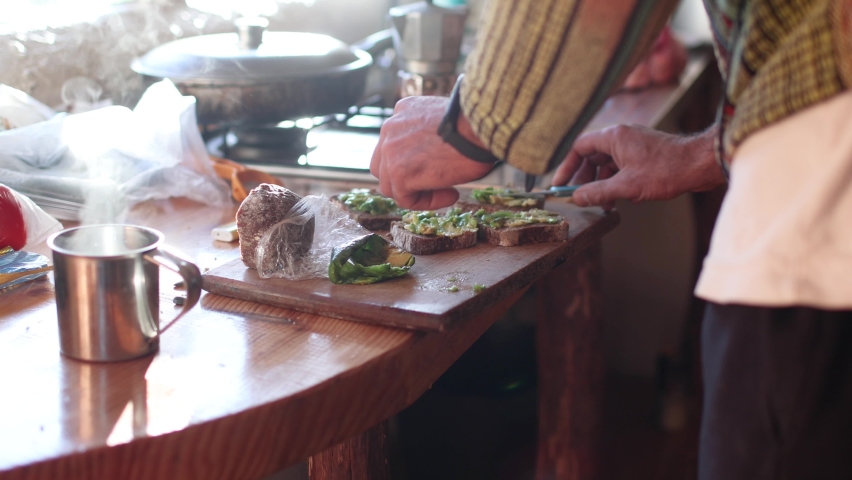 man preparing breakfast in the kitchen in the morning light. sandwich with avocado and coffee in lace