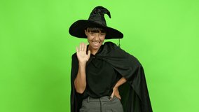 Young woman wearing witch hat for halloween parties saluting with hand with happy expression over isolated background. Green screen chroma key