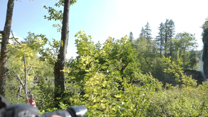Photographer taking picture of majestic waterfall hill with sun flare in Plitvice National Park