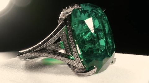 Green color emerald on ring jewelry close-up filming. Macro shooting of wealth trinkets and treasure gem stones. Color reflections of precious crystal minerals, fine cut emerald. Jewellery gemstones.