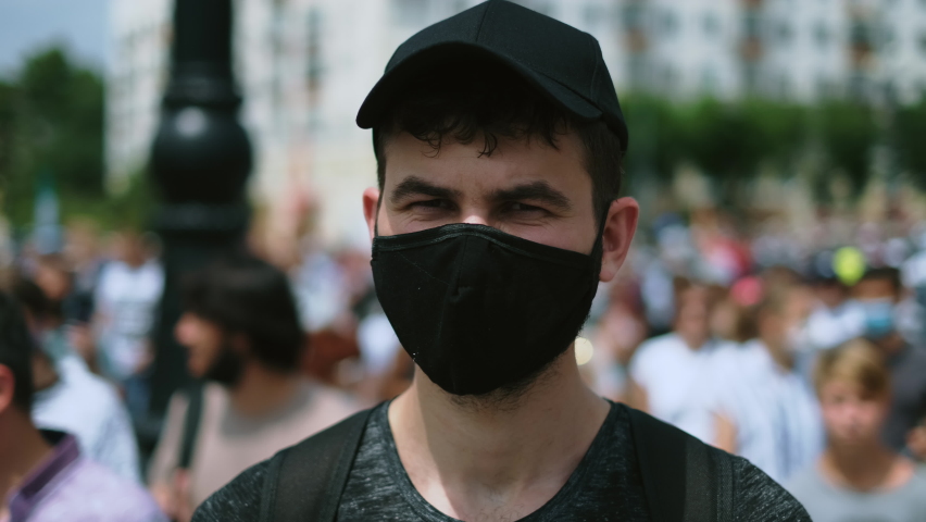 Anonymous riot activist picket. Rally strike man stands. Covid-19 demonstration guy in looks at camera. Masked political rebel in crowd. Opposition resistance revolt protester in coronavirus face mask Royalty-Free Stock Footage #1080370613