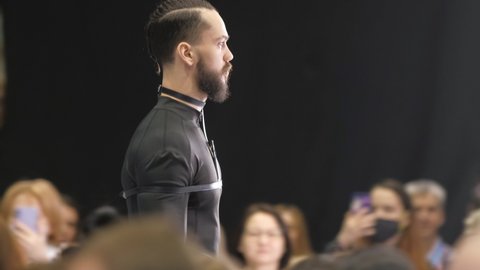 Beautiful male model walking down the runway podium. Men on fashionable expo week. Haute couture catwalk, elegant people vogue. Beauty guy catwalks on fashion show stage, delicate person defile look.