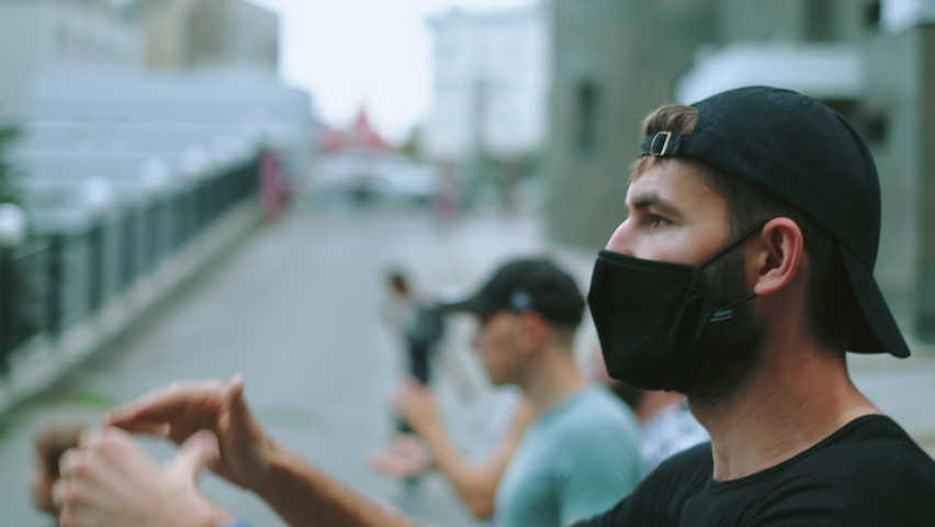 Masked rebel activist man in covid-19 regulations resistance picket crowd on rally revolt. Male protester on political riot demonstration. Opposition guy in restriction coronavirus facemask claps hand Royalty-Free Stock Footage #1080371195