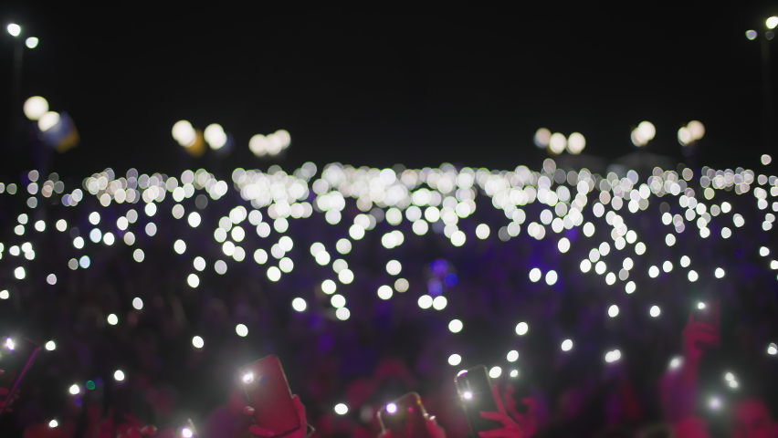 atmosphere of concert out of focus, unrecognizable fans holding mobile phones with flashlights in theirs hands in face of the stage Royalty-Free Stock Footage #1080371273