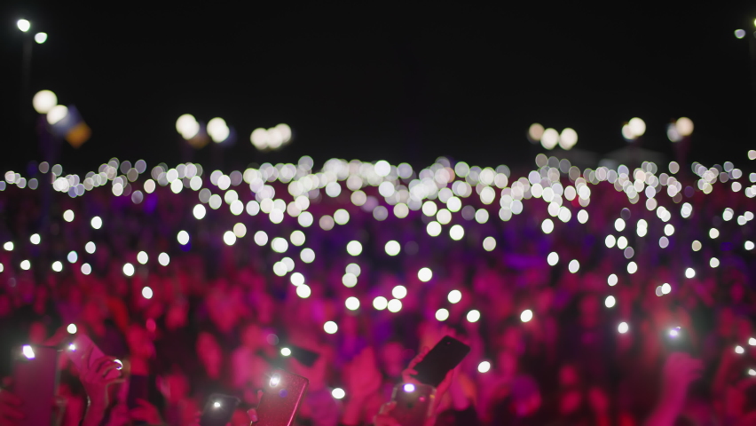 Atmosphere of concert out of focus, unrecognizable fans holding mobile phones with flashlights in theirs hands in face of the stage | Shutterstock HD Video #1080371273