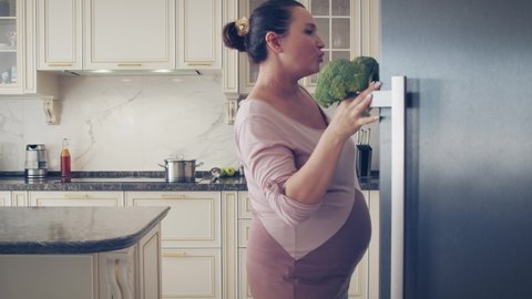 Pregnant mom listening music and relaxing stay at home. Cute fun mum dancing and preparing breakfast on kitchen. Concept pregnancy and happiness. Happy pregnant  woman singing in kitchen sunny day.