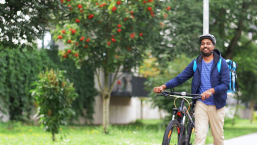 food shipping, profession and people concept - happy smiling delivery man with thermal insulated bag and bicycle walking along city street