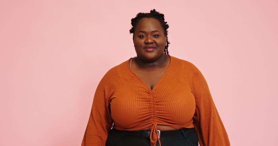 African American smiling plus size model rejoices showing thumbs-up gesture and poses looking into camera against pink wall slow motion | Shutterstock HD Video #1080380039