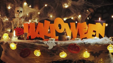 Skeleton and halloween word against scary horror dark background. Halloween decorations with spiders, cobwebs, candles and pumpkins. Halloween greetings