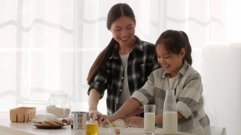 Chinese Mom And Daughter Baking Cake And Having Fun With Flour Touching Each Other's Noses Standing In Modern Kitchen At Home. Asian Family Of Two Bonding Cooking Together On Weekend