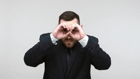 Bearded businessman in black official style suit looking through binoculars hand gesture with attentive view, observing far distance and zooming, spying. Indoor studio shot isolated on gray background - Powered by Shutterstock - Get 15% off with code: PIKWIZARD15