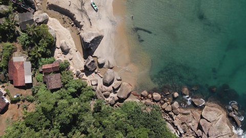 Aerial top view of a beautiful Brazilian beach. Tilt up on beach of turquoise water. Clear ocean. Boats on sand. Rocks and sea weed on water. Local community. River on the beach. 4K.
