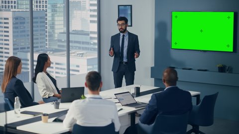 Diverse Office Conference Room Meeting: Male Project Manager Uses Green Screen Chroma Key Wall TV to Present Investment Opportunity for Investment Team. e-Commerce Product Strategy. Medium Wide