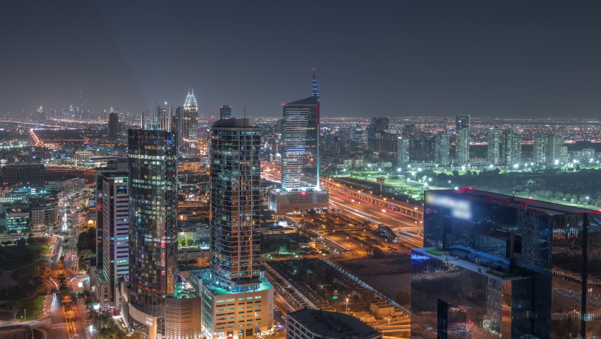 Aerial view of media city and al barsha heights district area night timelapse from Dubai marina. Towers and illuminated skyscrapers with traffic on a highway from above