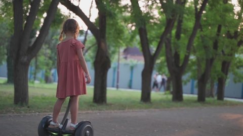 little girl riding hoverboard Scooter in the park on the way. child controls the Self-balancing scooters in summer. kid rides past friends on gyro scooter. new type of transport for children