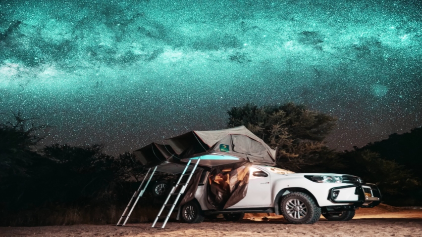 Astronomy Namibia starry landscape, travel in galaxy. Night timelapse of a safari vehicle in an adventurous wild camping location with a rooftop tent against the Milky Way and starry sky.