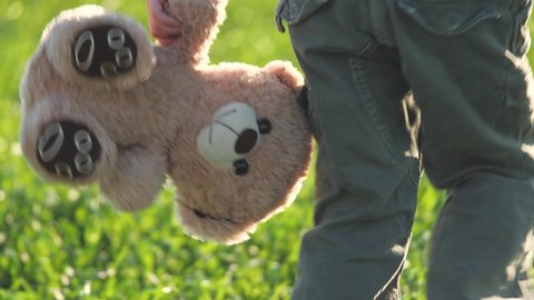 little boy carries a teddy bear in his hands, a kid with a teddy walks in park on a green lawn, development of children in a society of people, developmental delay and attention deficit in childhood