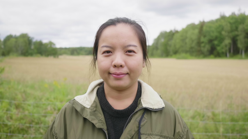 Front view of Asian female farmer standing in green field, portrait of woman farm worker in farming, smiling and looking at camera. Happy moods in a farm concept