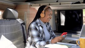 African senior woman using mobile phone and laptop inside mini van camper - Elderly black person enjoy technology 