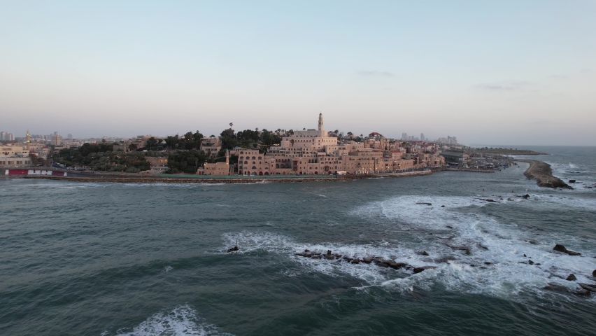 Aerial view low over waves and andromeda rocks, around the old Jaffa town, sunset in Tel Aviv, Israel - wide, panorama, drone shot
