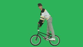 Extreme guy biker wearing hockey jersey standing on bmx bike over green screen background. Sporty young man rider have fun with bicycle on chroma key. 4k raw video footage