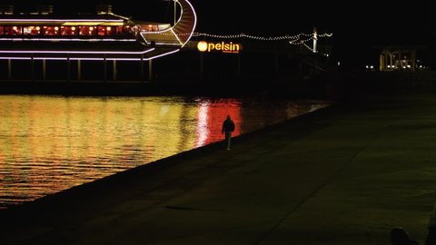 A man strolls along the Yalta seafront against the background of the Apelsin restaurant. The orange light of the lanterns is reflected in the sea.. Yalta, Republic of Crimea, April 26, 2021
