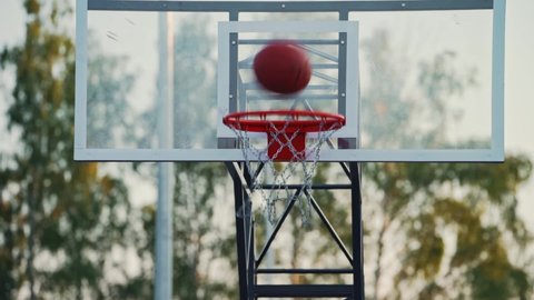 Outdoor basketball court. Street sports. Basketball ball hits into hoop. A lot of basketballs fly into a basketball basket. Training before the match. Practicing the accuracy of the throw. Warm up. 