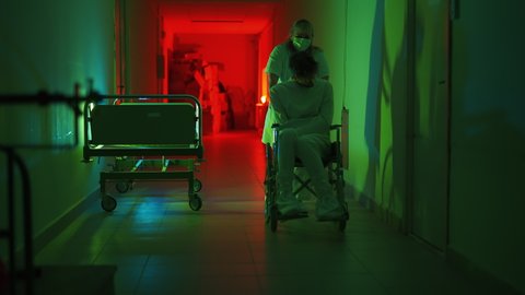 A paramedic is driving a mad male patient in wheelchair down corridor in mental hospital. Ill person in straitjacket is going crazy. Concept of paranoia or schizophrenia and madness or depression.
