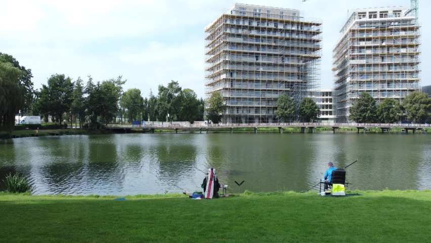 Two men fishing for carp at the stadionvijvers lake in the city park by a building under constuction