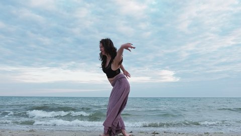 Dancing woman. Nature unity. Spiritual mediation. Back view of inspired graceful lady enjoying ocean breeze waves at sea beach horizon background.