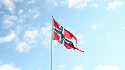 Waving national flag of Norway under a partly-cloudy sky.