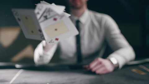 A professional croupier is working with cards. Close up of holdem dealer with playing cards on black table. Concept of casino gambling or poker and entertainment. Slow motion
