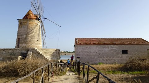 Paceco, Italy - 09 03 2021: Slow motion of family of tourists at Mulino Maria Stella windmill in front of saline in province of Trapani, Sicily. Italy
