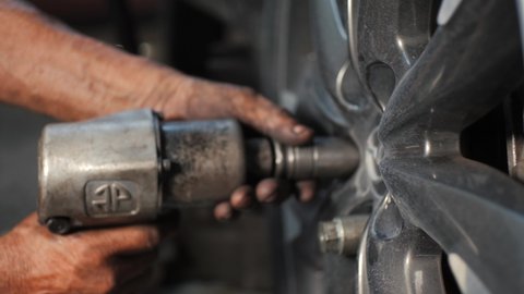 Latino Car Mechanic Using Tools Like Pneumatic Impact Gun For Tightening Cart Wheel Lug Bolts In Mexican Car Fix Garage - Slowmotion Close up
