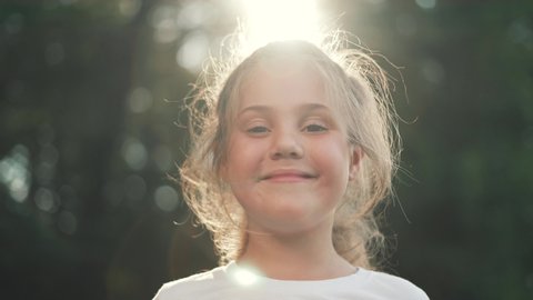 Happy girl in rays of the sun. Girl face in park close-up. Dream girl. Happy face of a child in rays of sun. Child smiles at camera. Girl dream. Face close-up. Happy child in park.Beautiful face