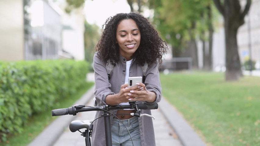 Young woman using smartphone in a city. Student girl with bicycle looking at mobile phone outdoor.  People, lifestyle, technology, travel, mobile apps, city life concept | Shutterstock HD Video #1080456044