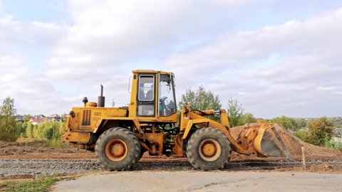 Belarus, Minsk - October 8, 2021: Tractor bulldozer drives close-up. Front-end loader using bucket. Road construction. Large excavator compacts rubble. Levelling driveway. Building site.