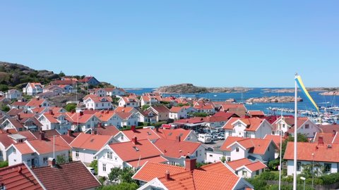 Coastal town in Sweden. West coast village by the ocean in aerial drone shot on sunny summer day. Fly over red rooftops picturesque white homes of Bovallstrand in Swedish Bohuslan Vastra Gotaland 