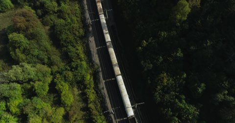 Freight long train carries with cargo carriages near river in wild mountains landscape through a difficult part of Trans Siberian railways. Aerial drone wide into the distance view at summer sunny day