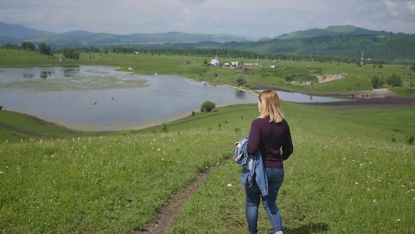 Teamwork. A group of tourists walks through a green field in a mountainous area. Walking tour of youth at the foot of the mountain.