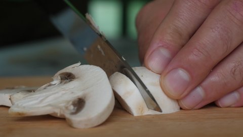 Close-Up Man Cutting Champignons on Wooden Cut Board. Diet Healthy Eating. Macro Shot Male Hands Cutting Champignon Mushroom By Knife on Wooden Board. Vegetarian Healthy Food. Diet Healthy Lifestyle.