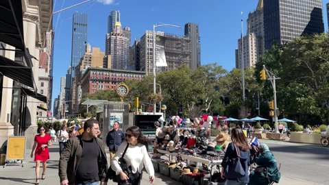 NYC, USA - OCT 6, 2021: people walking past street vendor selling hats in Flatiron with 5th Avenue Clock in Manhattan New York City.